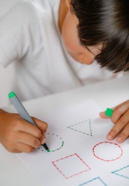 Preschooler boy sitting at the desk, drawing shapes